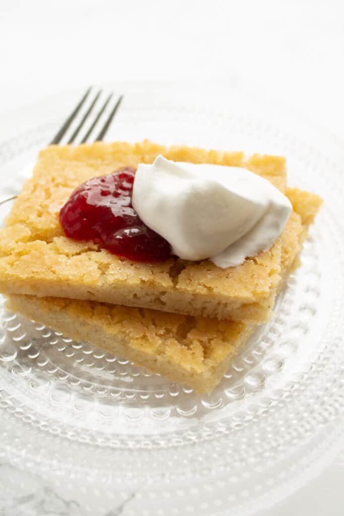 A pile of pancakes on a plate with fresh raspberries and whipped cream