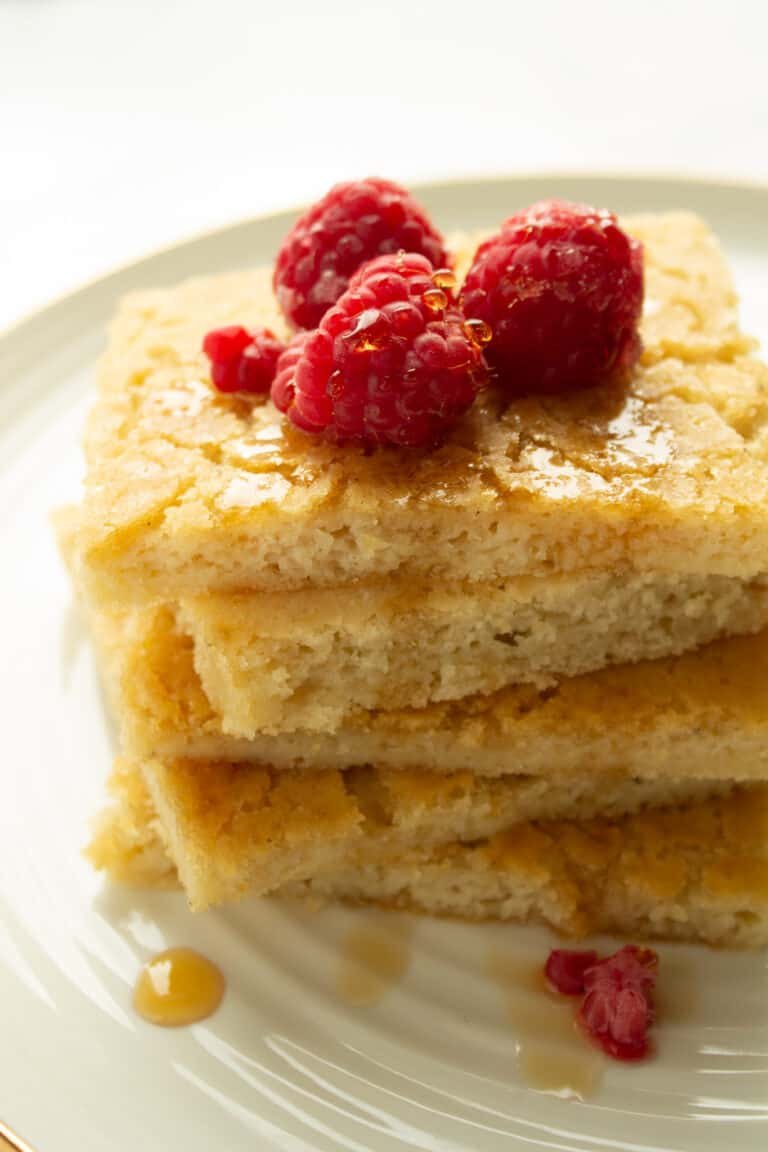 A pile of pancakes on a plate with fresh raspberries and syrup
