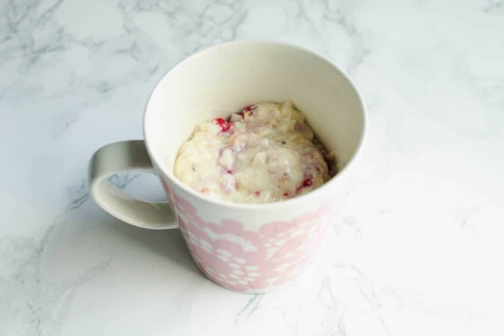Cake dough in a mug with raspberries and coconut